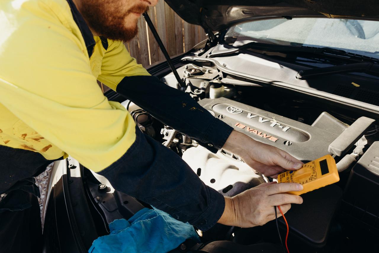 Mechanic checking engine with multimeter during inspection